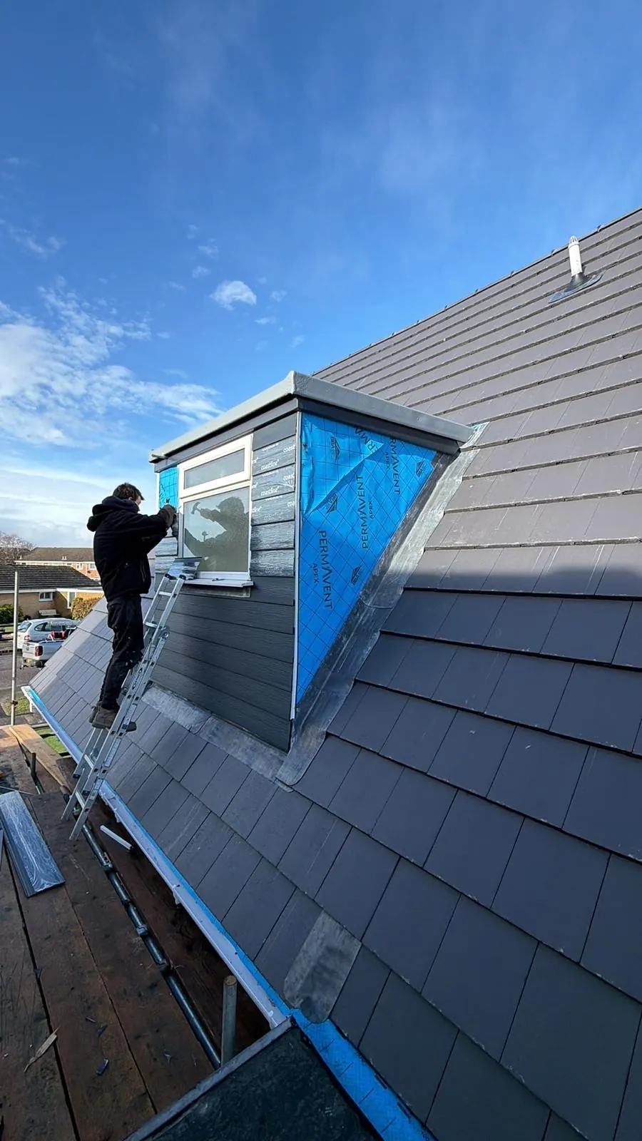 Roofer working beside a new dormer on a grey tiled roof