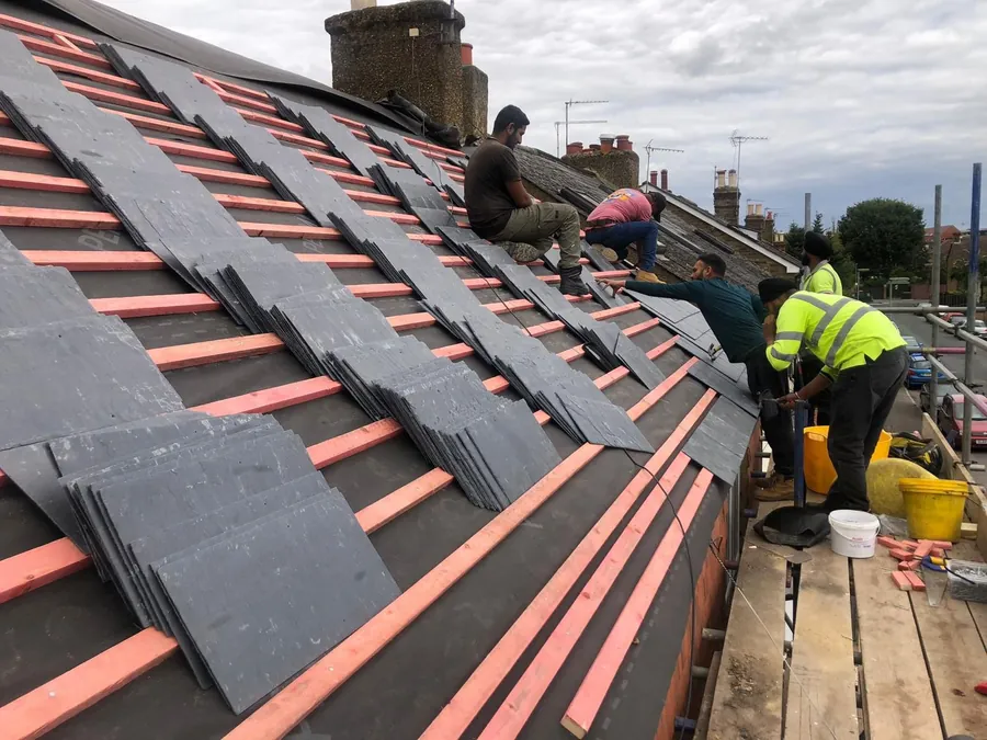 Roofers fixing new slates over red battens and membrane